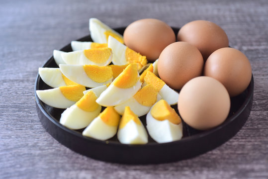 Slice boild eggs with unopened egg in  black wooden plate
