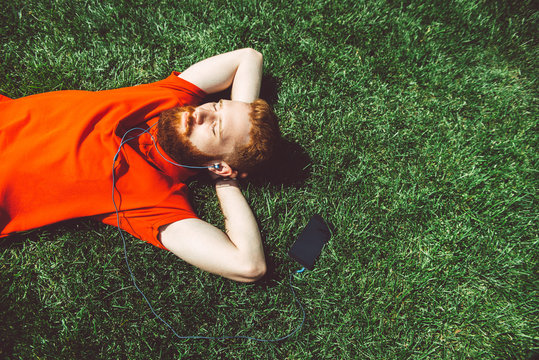 Attractive Guy Model Is Lying On The Grass And Listening To Music.