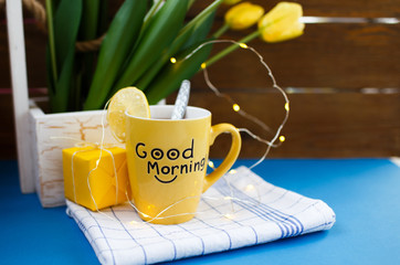 Photo of a yellow cup with tasty tea, table setting for Easter, tea mug on a blue background, holiday decoration with tulips