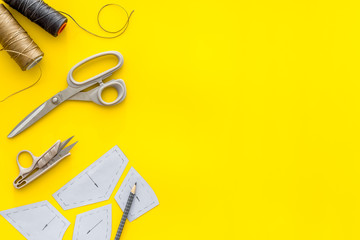 Clothes designer work desk. Pattern, scissors, thread on yellow background top-down copy space