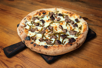 Freshly baked pizza with cheese, sauce, vegetables and meat on a wooden table