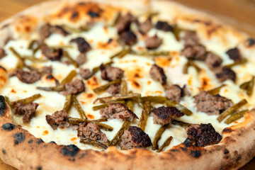Freshly baked pizza with cheese, sauce, vegetables and meat on a wooden table