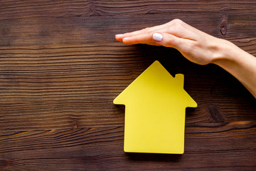 Property insurance concept. Hand defends house cutout on dark wooden backgound top view copy space