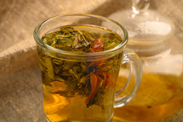 Flower tea brewed in a glass Cup, a glass teapot with flower tea on a background of rough homespun fabric. Close up.