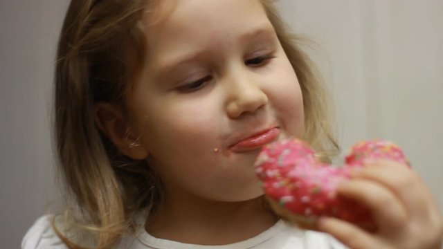 Child mouth bites rose donut. Closeup baby girl eating doughnut with glase. Delicious, sweet, sweettooth.