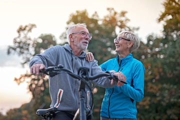 Older couple in park, he is with bicycle and she walk beside and talking
