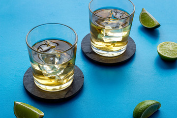 Whiskey with ice. To glasses of strong alcohol drink near lime on blue background