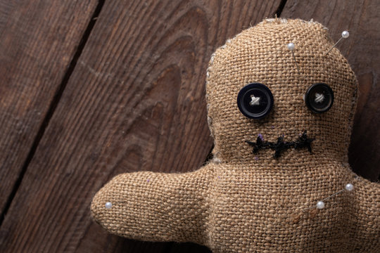 Voodoo doll on a wooden background with dramatic lighting. The concept of witchcraft and black art. Burlap doll on a wooden background. Pierce with maces. Copy space.