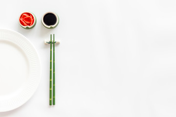 Tableware for sushi and rolls. Plate, chopsticks, small bowls with ginger and sause on white background top-down copy space
