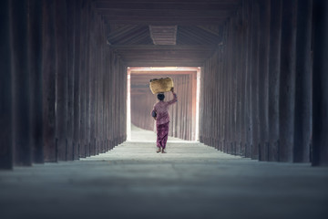 Woman walks along the walkway with baskets on head in temple, north region of Myanmar, Myanmar