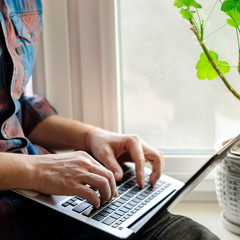 A man sits on a window sill with a laptop in his hands and works