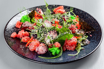 Italian Cuisine. Seafood salad with octopus, lettuce, grapefruit, green moss, black and white sesame seeds, red pepper. background image, copy space text