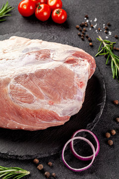 A large piece meat of raw pork, hip or tenderloin on a black background with vegetables and spices, background image, copy space text