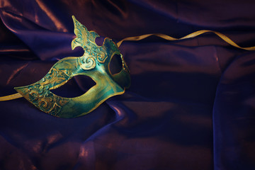 Photo of elegant and delicate gold and green Venetian mask over purple silk background