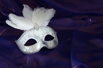 Photo of elegant and delicate white Venetian mask over purple silk background