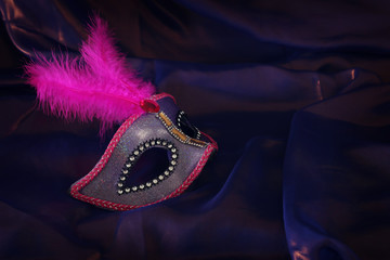 Photo of elegant and delicate pink Venetian mask over purple silk background