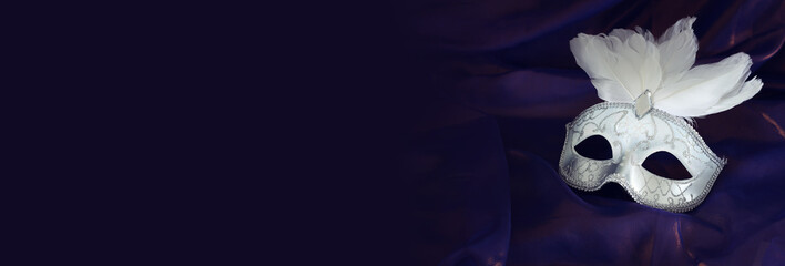 Photo of elegant and delicate white Venetian mask over purple silk background