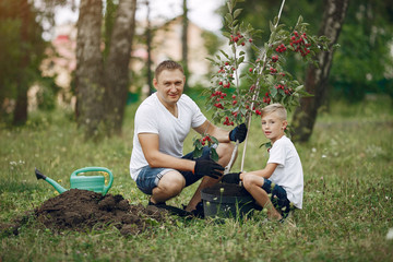Naklejka na ściany i meble Family on a yard. Father with son planting a tree. Boy with a green funnel