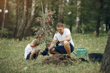 Family on a yard. Father with son planting a tree. Boy with a green funnel