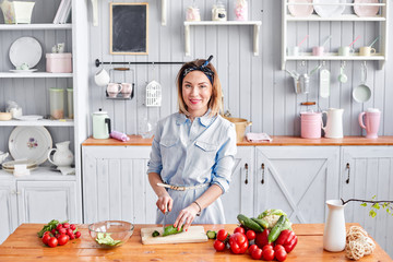 Beautiful young woman is preparing vegetable salad in the kitchen. Healthy Food. Cooking at home. Dieting Concept.