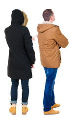 Back view of couple couple in winter jackets pointing.