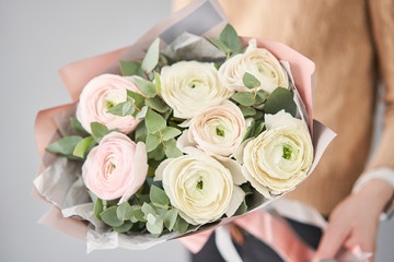 Obraz na płótnie Canvas Persian buttercup in womans hands. Bunch pale pink ranunculus flowers with green eucalyptus. The work of the florist at a flower shop