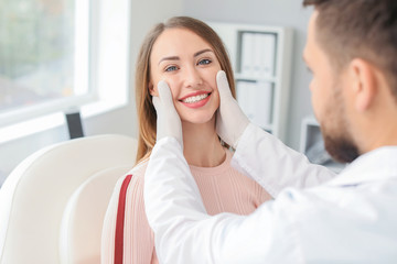 Plastic surgeon examining young woman's face prior to operation in clinic