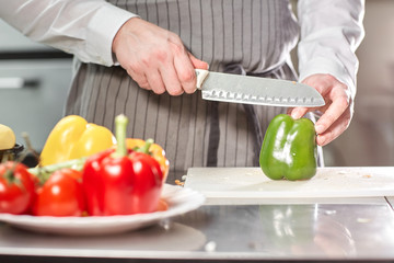Closeup of hand with knife cutting fresh vegetable. Young chef cutting beet on a white cutting board closeup. Cooking in a restaurant kitchen