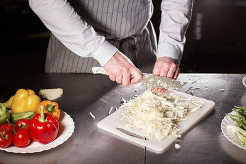 Closeup of hand with knife cutting fresh vegetable. Young chef cutting beet on a white cutting board closeup. Cooking in a restaurant kitchen