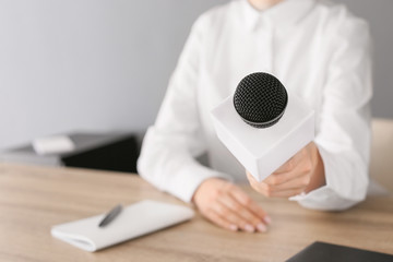 Female journalist with microphone having an interview in office, closeup