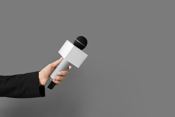 Journalist's hand with microphone on grey background