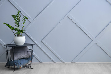 Stylish basket with pillows and houseplant near grey wall