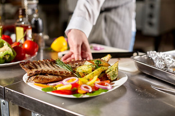decorated with a sprig of rosemary. the chef prepares in the restaurant. Grilled rack of lamb with fried potatoes and fresh vegetables