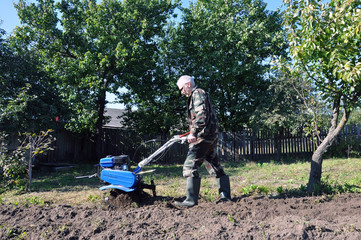 plowing the land in the garden with a cultivator. a man plows the land with the help of motor cultivator.