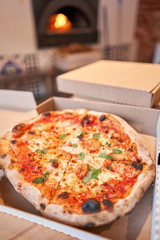 Pizza delivery concept. Baked products in a cardboard box against a wooden background. Baked tasty margherita pizza in Traditional wood oven in Neapolitan restaurant, Italy.