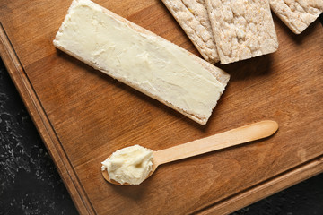 Spoon with tasty cream cheese and crispbread on wooden board