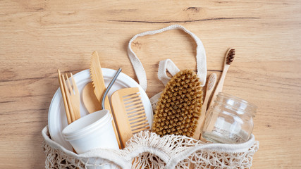 Fototapeta na wymiar Zero waste concept. Cotton String Shopping Bag with Eco-Friendly kitchenware and bathroom items. Top view shopper with bamboo cutlery set, comb, spa brush, glass jar, toothbrushes on wooden table