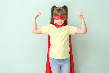 Little girl in superhero costume on color background. Concept of feminism