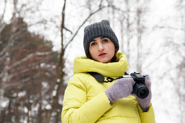 Young woman with a camera in a winter park on a background of trees. Women hobbies. Copy space