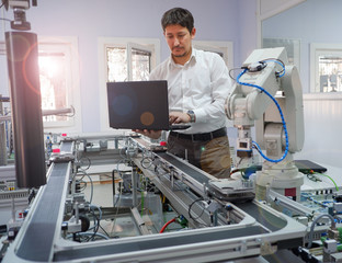 Close-up of Engineer is working on laptop to programming smart factory automation and automated car on production line is waiting. Industry 4.0 concept; artificial intelligence in smart factory.