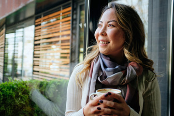 Beautiful Asian woman with tablet in café looking away.