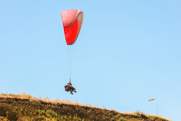 Tourist pair flight on a red paraglider in blue sky above the earth