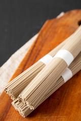 Uncooked Buckwheat Soba Noodles on a rustic wooden board on a black background, low angle view. Copy space.