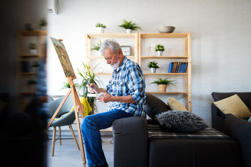 Smiling mature man painting on canvas at home