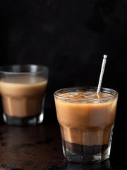 Two glasses of coffee with milk, a cooling drink is iced coffee. The glass is located on a dark metal background. Close-up, vertical orientation, space for text. Shallow depth of field.