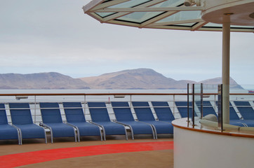Blue sun loungers or deck chairs lined up on cruiseship or cruise ship liner with red jogging track...