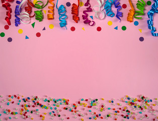 The concept of birthday. Border of colored paper ribbons and confetti on a pink background. Free space.