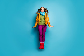 Full size photo of pretty funny lady jump high up rejoicing good mood wear casual yellow overcoat scarf violet pants red boots green pullover isolated blue color background