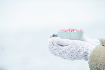 Fototapeta na wymiar Female hands holdink white cup of coffee with white and pink marshmallows