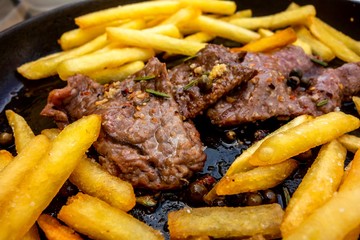 Fried spicy pork steaks with french fries in pan.